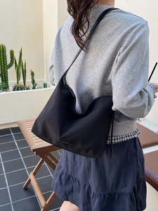 Minimalist black nylon crescent shoulder bag shown on model in a natural outdoor setting