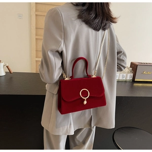 Detail of red velvet handbag with pearl chain and gold ring clasp on grey blazer