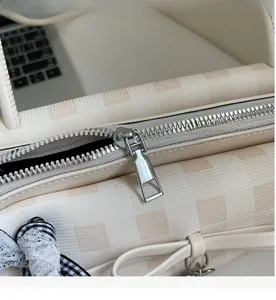 Detail of silver smooth zipper and cream checkered texture on a commute shoulder bag