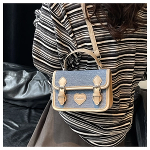 Detailed view of denim crossbody bag with beige leather trim and fashion heart patch