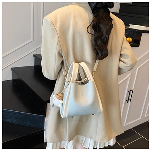 Detail of light blue crossbody basket bag with plush charm on a model in elegant indoor setting
