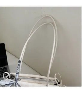 Detail of cream tote bag featuring long handles, plaid ribbon, and lace trimming