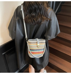 Detail of colorful woven straw bucket bag with blue leather strap on model's back