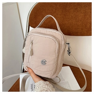 Detail of light beige nylon crossbody bag with multi-zipper layers on a brown velvet seat