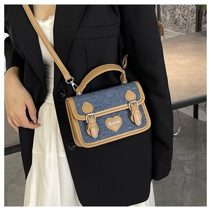 Detail of denim crossbody bag with leather trim and heart patch worn by a model
