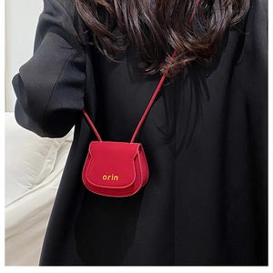 Close-up of a mini red leather saddle bag with yellow orin logo on a black blazer