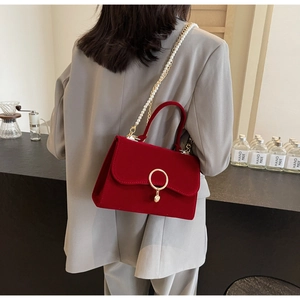 Detail of red velvet crossbody bag with gold ring closure and pearl chain strap on model