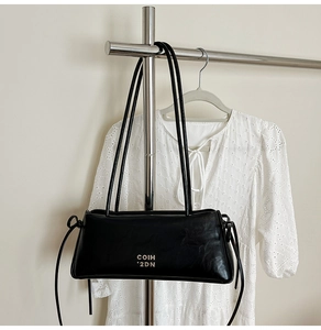 Détail d'un sac à bandoulière noir en similicuir avec lettrage blanc et nœuds latéraux