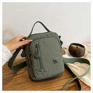 Detail view of olive green nylon crossbody bag with multi-zipper pockets and metal logo