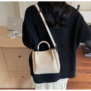 Close-up of beige lychee grain leather bucket bag with top handle and logo detail