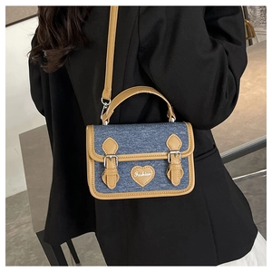 Close-up of small denim crossbody bag with tan leather trim worn by a model in a suit