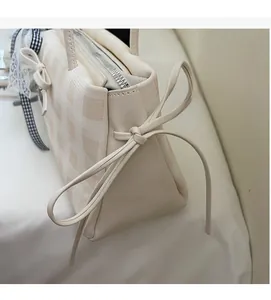 Close-up of cream checkerboard shoulder bag featuring a side leather bow detail