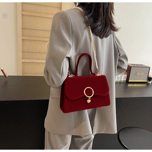 Detail view of red velvet handbag with gold ring clasp and pearl chain worn by model