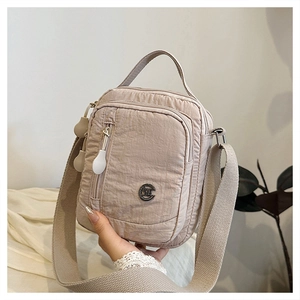 Macro shot of a beige nylon crossbody bag featuring multiple zipper pockets and wide strap