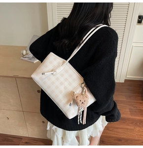 Detail of cream checkered tote bag featuring a leather texture and brown plush bear charm