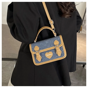 Detail of denim crossbody bag with brown leather trim and fashion heart patch detail
