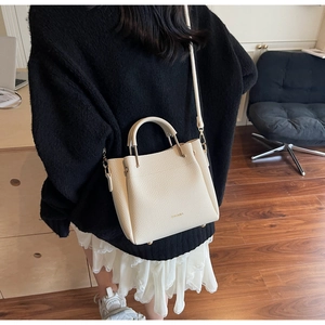 Detail view of cream bucket bag with lychee grain leather and metal logo lettering