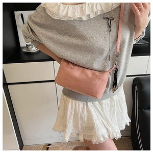 Detail of pink suede crossbody bag with thin shoulder strap and silver metal hooks
