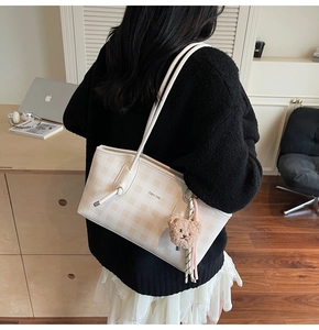 Detail view of a cream checkered tote bag with plush bear charm and thin leather strap