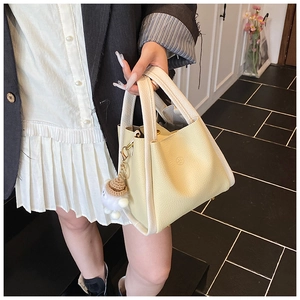 Detail of yellow lychee leather bucket bag with cute plush bear and round logo