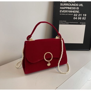 Detail of burgundy velvet handbag with golden hardware and pearl chain on marble surface
