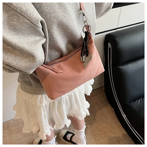 Macro view of peach suede crossbody bag with heart charm and black fringe tassel