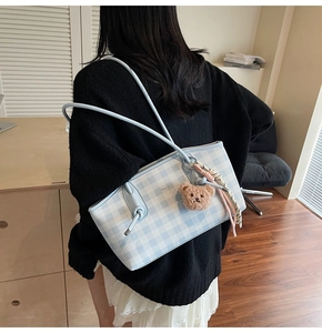 Blue and white gingham tote bag with cute bear charm worn by model in a soft room