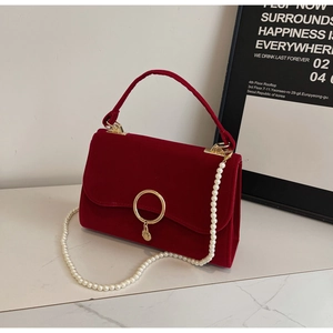 Detail of red velvet handbag with golden ring buckle and elegant white pearl strap