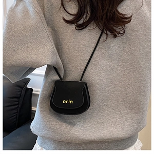 Minimalist black leather saddle bag with yellow logo detail worn by a model