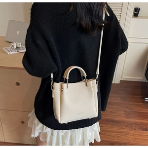 Detail of off-white lychee grain leather handbag with gold logo and dual handles