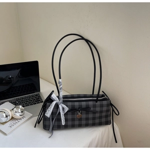 Detail of grey checkered shoulder bag featuring lace bows and heart pendant with a laptop