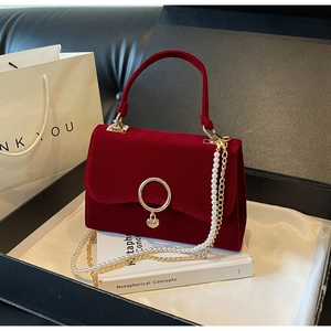 Macro detail of red velvet handbag with pearl chain and heart charm in a premium gift box