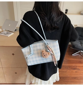 Detail of light blue checkered tote bag featuring a cute brown plush bear charm and woven cord