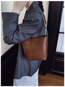 Détail du sac seau tressé marron foncé avec motif damier sur un blazer gris chic