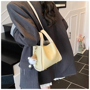 Close-up of a light yellow lychee leather bucket bag with contrast trim and plush charm