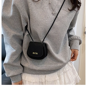 Detail of a mini black saddle bag with yellow branding on a casual outfit model