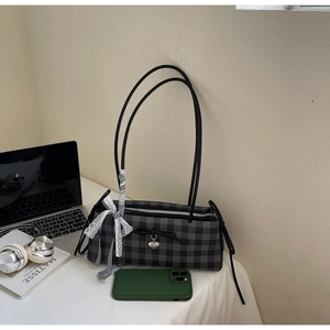 Close-up of a grey plaid shoulder bag featuring a silk bow and heart pendant detail