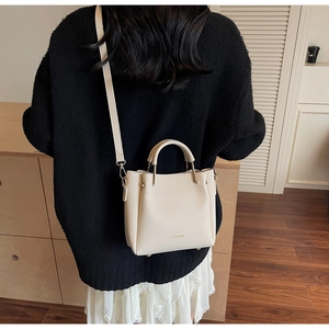 Detailed shot of beige lychee texture leather bucket bag with gold hardware on model
