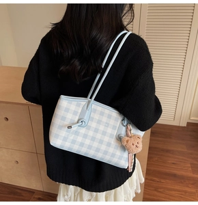 Detail of checkered tote bag with brown plush bear charm and slender shoulder straps