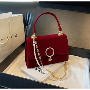 Detail of red velvet handbag featuring a gold round lock and elegant heart pendant