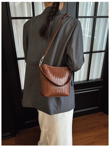 Détail du sac seau marron tressé avec étiquette logo et finitions métalliques élégantes
