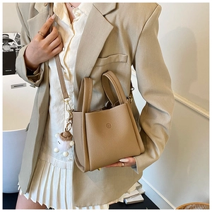 Detail of tan lychee grain leather tote bag with embossed logo and plush charm
