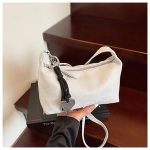 Detail of white suede underarm bag with silver zipper and heart-shaped metal pendant