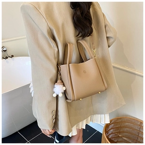 Detail of camel bucket bag with lychee leather texture and plush charm accessory