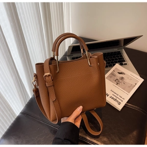 Close-up of brown litchi grain leather bucket bag with gold hardware on an ottoman