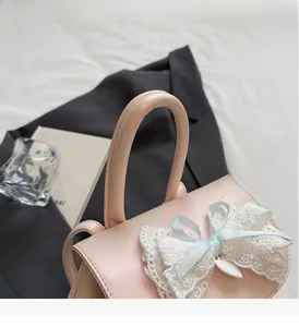 Detail of pink faux leather handbag with lace bow and thick cylindrical handle