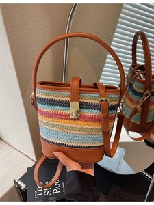Colorful hand-woven straw bucket bag with brown leather handles and adjustable shoulder strap