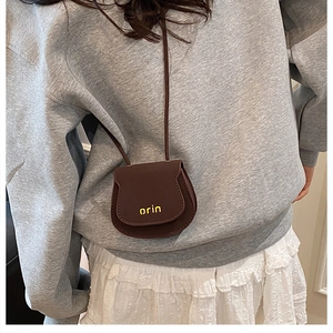 Detail of dark brown mini saddle bag with yellow orin logo and slim neck strap
