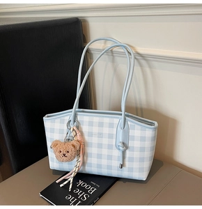 Close-up of a blue gingham tote bag with a brown plush bear and ribbon charm