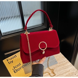 Detail of red velvet handbag with gold ring clasp and chain strap held by hand